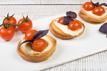 bruschetta with basil leaves and red cherry tomatoes on white basalt board on white wooden background