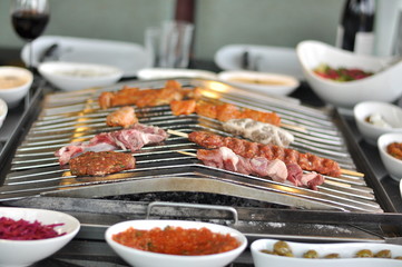 Traditional Cypriot meze and mix meat and chicken kebab table with charcoal barbecue on the table for self cooking during the eating time