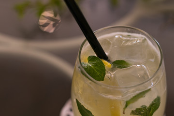 Mojito cocktail with yellow lemon, green mint leafs and black straw on glass table. Close up. Top...