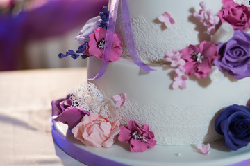 Obraz na płótnie Canvas Beautiful fondant covered wedding cake decorated with edible lace and bouquet of purple lilac and pose flowers. Close-up.
