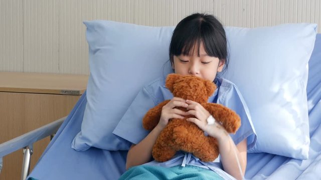 Little girl resting in hospital while hugging her teddy bear in hand. People with Healthcare and Medical Concept.