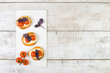 bruschetta with basil leaves and red cherry tomatoes on white basalt board on white wooden background