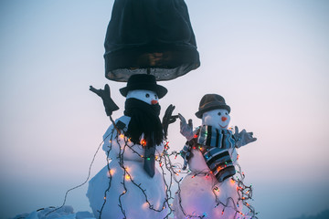 Happy New Year congratulations, couple of snowmen waiting for guests, Christmas decorations in the garden of a family home. Beautiful snowmen in hats near the lamp, coziness for the holidays
