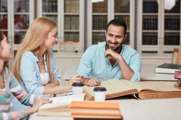 Happy young university students studying with books in library. Group of multiracial people in college library.