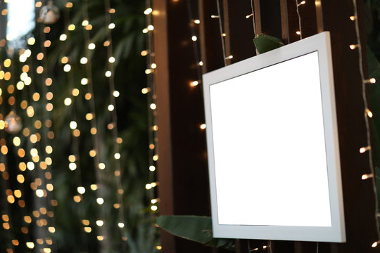 Empty blank photo frame in christmas decorated defocused background .Blank photographs hanging on a clothesline against a Bokeh lights background. Blank frame with sparkling gold bokeh wall.