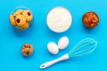 Cook cookies at home concept. Ingredients and instruments for make cookies. Fresh cookies near flour, eggs and whisk on blue background top view