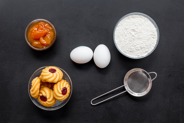 Cook cookies at home concept. Ingredients and instruments for make cookies. Fresh cookies near flour, eggs and sieve on black background top view