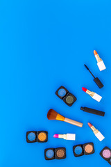 visagiste desk with decorative cosmetics: eyeshadows, lipstick, brush blue background top view space for text