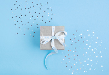 Christmas gift with blue ribbon on blue pastel background with festive decorations. Christmas background with copy space.