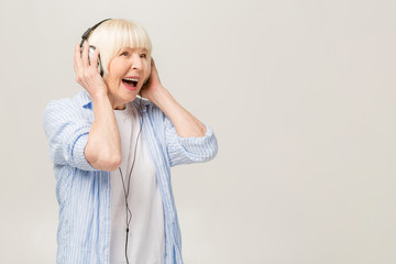 Elderly happy surprised woman with headphones listening to music on a phone isolated on white background.