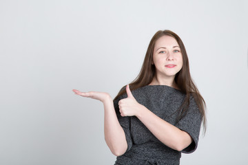 Young cute woman showing thumbs up over gray background. Looking at camera