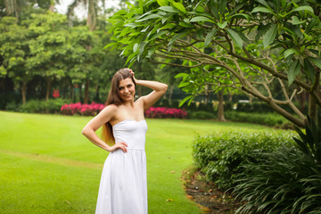 portrait of carefree young woman in white dress posing in green summer park