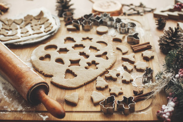 Christmas gingerbread cookies dough with metal cutters on rustic table with wooden rolling pin, cinnamon ,anise, cones, christmas decorations. Atmospheric stylish image, winter holidays