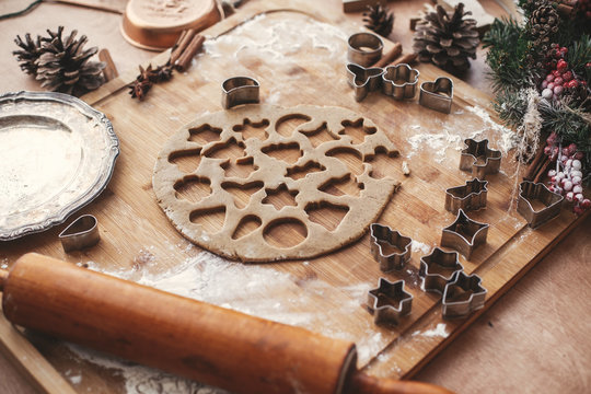 Christmas gingerbread cookies dough with metal cutters on rustic table with wooden rolling pin, cinnamon ,anise, cones, christmas decorations. Atmospheric stylish image, winter holidays - Powered by Adobe
