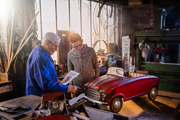 A grandfather and his grandson restoring an old pedal car