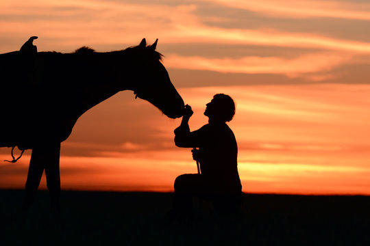 Love horse rider stroking horses nose at beautiful idyllic sunset. Romantic background with favorite horse and man silhouette. 