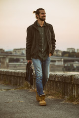 Handsome modern businessman with laptop bag walking by the river.