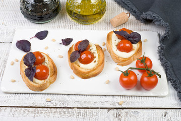 bruschetta with basil leaves and red cherry tomatoes on white basalt board on white wooden background