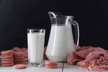 A glass of milk, a jug and a delicious cookie on a white, wooden table and a black background