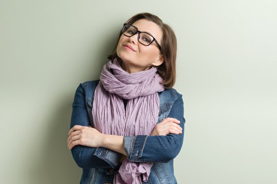 Portrait of smiling middle aged confident woman in glasses with folded arms, green wall background, copy space