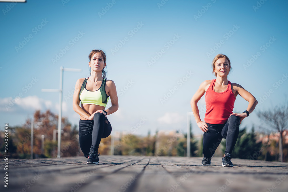 Wall mural Two beautiful women perform outdoor exercise in park.