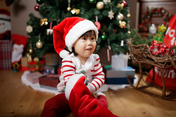 toddler baby girl wearing santa claus costume looking for gift  in front of christmas tree