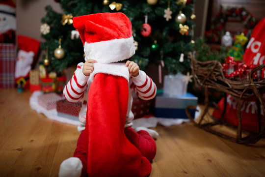 toddler baby girl wearing santa claus costume looking for gift  in front of christmas tree
