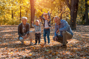 Grandparents and grandchildren throwing leaves in park and having fun together - obrazy, fototapety, plakaty