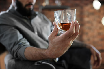 Man with glass of whiskey indoors, closeup