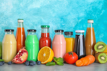 Bottles with different drinks and ingredients on table against color background
