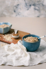Oatmeal Porridge in a Blue Bowl with Raw Oats and Brown Sugar in Background