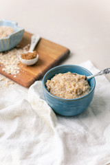 Oatmeal Porridge in a Blue Bowl with Raw Oats and Brown Sugar in Background