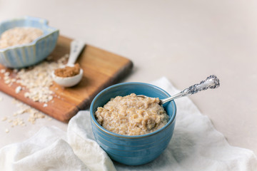 Oatmeal Porridge in a Blue Bowl with Raw Oats and Brown Sugar in Background