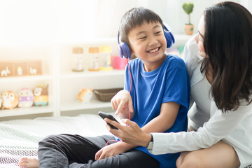 Mother with son listening to music on bed in bedroom