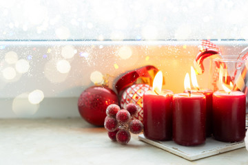 Christmas styled scene with four red burning candles on windowsill with frozen window with bokeh lights