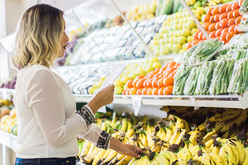 Obraz premium young woman holding shopping list with fruits background in supermarket