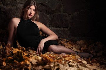 Autumn mood. Beautiful young gril in black dress lying on the autumn yellow leaves. Seasonal autumn fashion