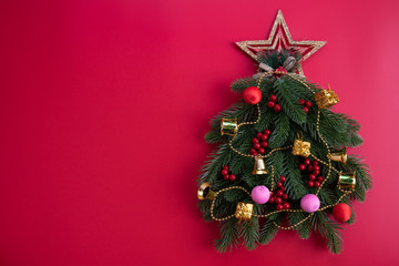 Christmas background concept. Top view of Christmas tree with spruce branches, pine cones, red berries and golden star on red background.