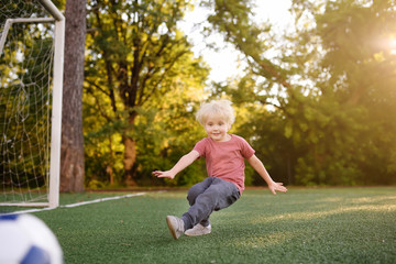 Little boy having fun playing a soccer/football game on summer day. Active outdoors game/sport for children.