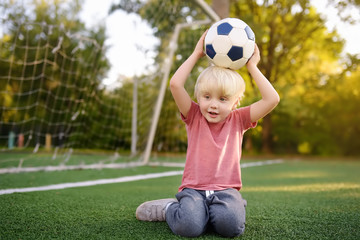 Little boy having fun playing a soccer/football game on summer day. Active outdoors game/sport for children.