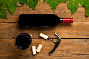 Wine bottle opener glass stoppers and vine leaves on wooden background. Top view with copy space.