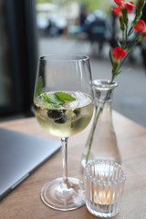 Glass of alcoholic drink with peppermint and grapes next to a vase of flowers.