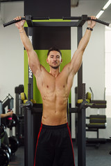 Fototapeta premium Strong attractive man does pull-up on the crossbar during training in the modern gym. Front view.