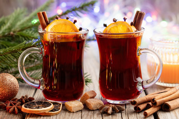 Glass mugs of hot mulled wine with spices and citrus fruits, Christmas tree branches and bokeh...