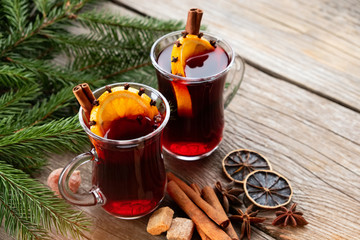 Glass mugs of mulled wine with spices, citrus fruits and Christmas tree branches on wooden table....