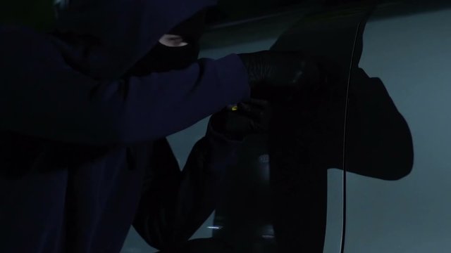Thief in dark mask breaking lock on cars door, night time hijacking crime