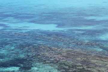 Looking down at the green, blue, and turquoise waters of the Caribbean Sea, Montego Bay, Jamica. A rocky sea bed can be seen in the shallow area.