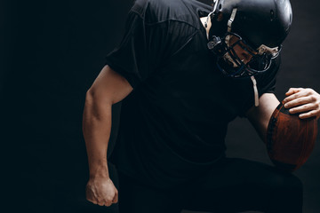 American football player with helmet and armour standing on one knee bending over the ball on...