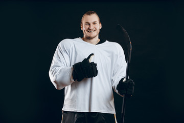 Naklejka premium Portrait of cheerful handsome hockey player getting into the mood for winning before game starts. Sportsman in white uniform smiling at camera isolated on black