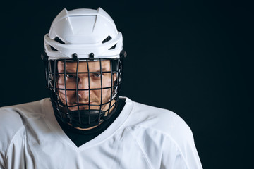 Head and shoulder portrait of confident brave hockey player in white uniform with protective helmet...